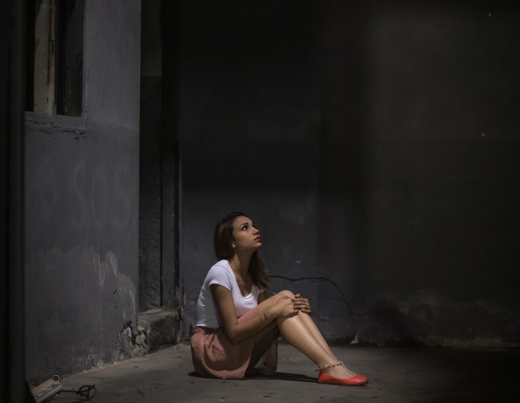 Young woman locked alone in a dungeon looking up to a window