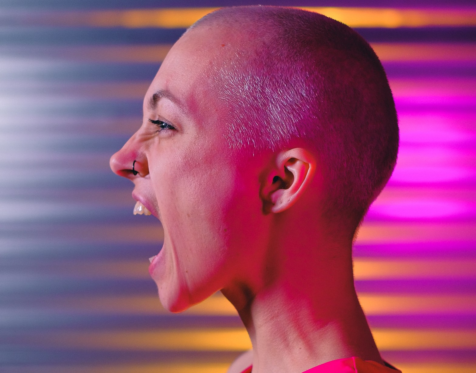 A woman with a shaved head shouting against an abstract, colorful background